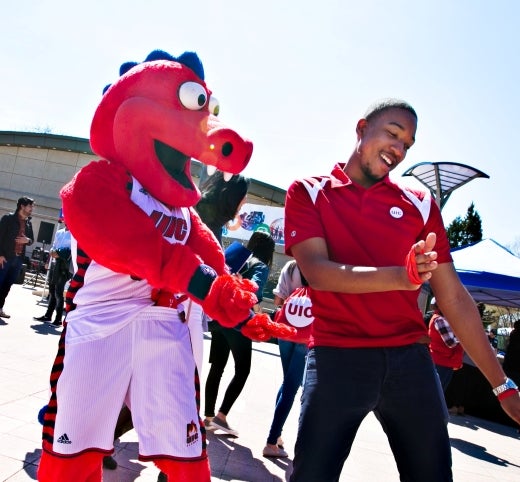 A student dancing with Sparky the Dragon, the UIC mascot